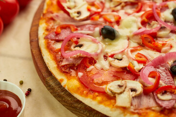 Freshly baked pizza with smoked sausages, red pepper, mushrooms, onion and olives served on wooden background with tomatoes, sauce and herbs. Food delivery concept. Restaurant menu