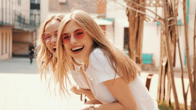 Two young beautiful blond smiling hipster girls in trendy summer clothes. Sexy carefree women posing on street background. Positive models having fun. Showing good relationship. Hugging