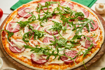 Freshly baked tasty pepperoni pizza with salami, mozzarella cheese and rukkola served on wooden background with tomatoes, sauce and herbs. Food delivery concept. Restaurant menu