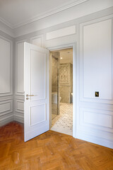 view of open door to marble bathroom, luxury interior design with white paneled walls and parquet floor