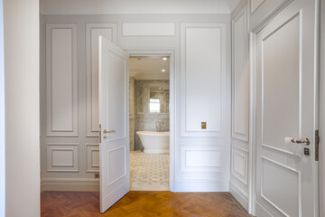 view of open door to marble bathroom, luxury interior design with white paneled walls and parquet floor