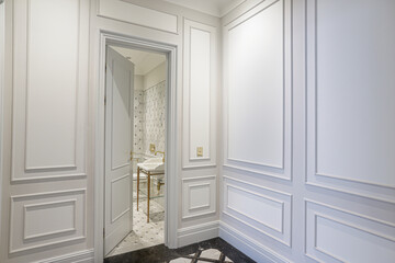 view of open door to marble bathroom, luxury interior design with white paneled walls and parquet floor