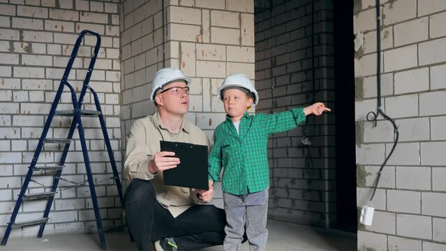 The boy and his father came to the construction site and are thinking about what repairs to make in the children's room. A boy and an adult man in construction helmets. High quality 4k footage
