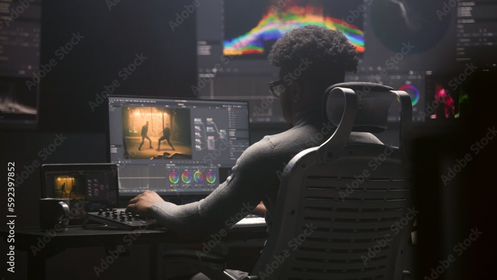Fototapete African American film editor does color grading on computer in modern studio. Big monitors with RGB colour correction graphic bar and program interface on the wall. Video post production. Handheld.