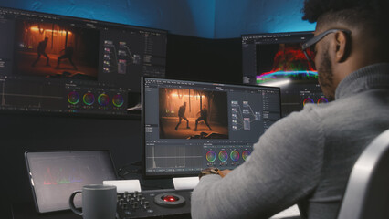 African American colorist makes color grading on control machine in modern studio. Big screens with...