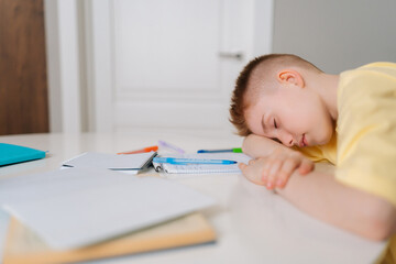 Close up side view of exhausted pupil boy sitting at home or classroom lying on desk filled with books training material and notebook. Tired schoolchild sleeping lazy bored to study lack of energy.