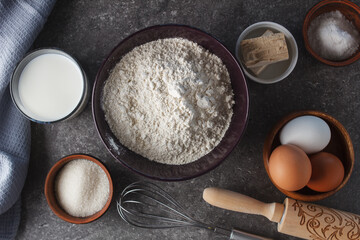 Preparation for baking. Eggs, sugar, milk, flour, salt, yeast, rolling pin, whisk on the kitchen table.