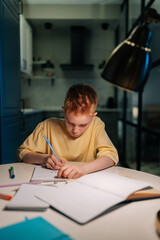 Vertical portrait of pupil student boy studying at home writing in exercise book doing homework,...