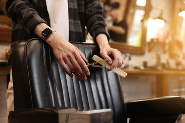 Hair style, hairdresser, beauty and customer service concept. Cropped shot of barber man hands hold professional stylish gold hairbrush and scissors by the workplace, leather black chair in barbershop