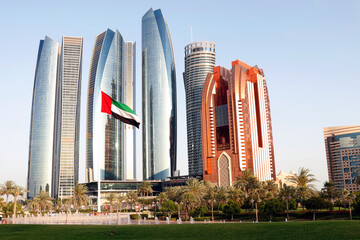 united arab emirates (uae) national flag waves on air in the sky in front of tall buildings in abu...