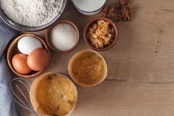 Preparation for cooking sweet pastries. Dough, eggs, sugar, milk, flour, salt, candied fruits, raisins, nuts, whisk on the kitchen table. copy space