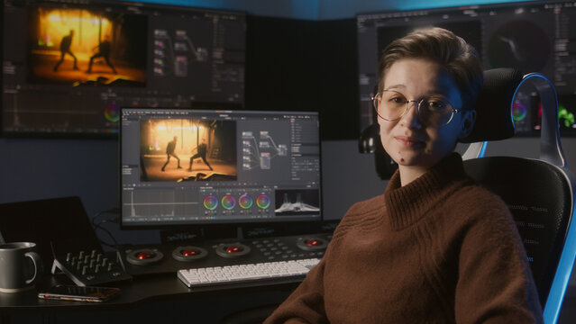 Young female video editor records for blog, talks about films color correction. Software interface with color wheels and movie footage on computer monitor and big screens. Color grading control panel.