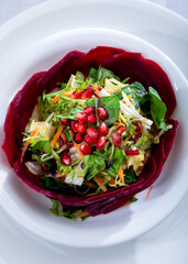 Healthy vegetarian salad, roasted root vegetables, and pomegranate seeds. Fresh mix salad leaves, carrot, and pomegranate seeds. Top view.