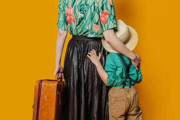 Back side view on stylish woman with son and suitcase on yellow background