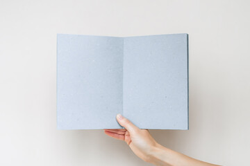 a female hand holds an open blue notebook with blank pages on a gray background
