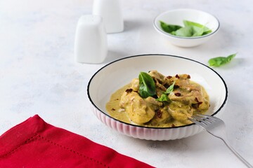 Pieces of stewed chicken in basil pesto sauce in a white plate on a light concrete background.