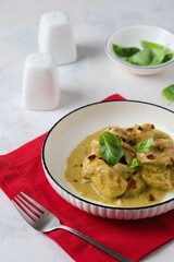 Pieces of stewed chicken in basil pesto sauce in a white plate on a light concrete background.