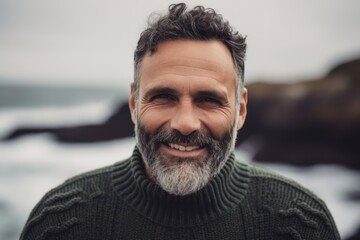 Portrait of a handsome mature man with gray beard and mustache wearing a green sweater on the beach