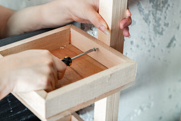 Detailed view of a woman's hands disassembling a wooden shelf with a screwdriver.
