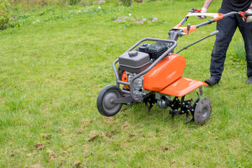 Obraz premium A man works the land in the garden with a cultivator, prepares the soil for sowing. farming concept.Garden tiller to work, walk-behind tractor.plow the field with a farm tractor