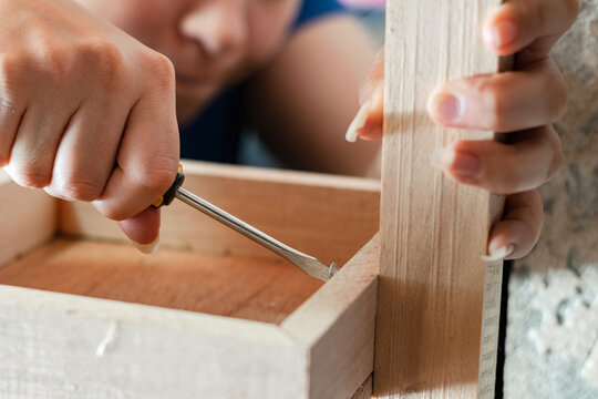 detailed view of a woman's hands, grasping a screwdriver to disassemble a wooden rack