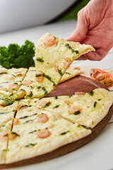 The human hand takes Freshly baked tasty pizza with shrimps and mozzarella cheese served on wooden background with tomatoes, sauce and herbs. Food delivery concept. Restaurant menu