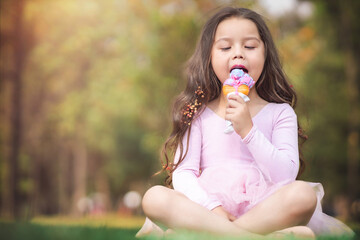 Cute blonde curly-haired girl eating a nice ice cream in the park, concept of children's day, copy space