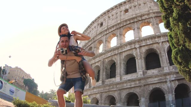 Lovely young couple at Colosseum, piggyback spreading arms at sunrise. Rome, Italy.