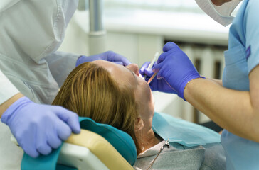 A doctor examines a woman's teeth with a dental instrument.