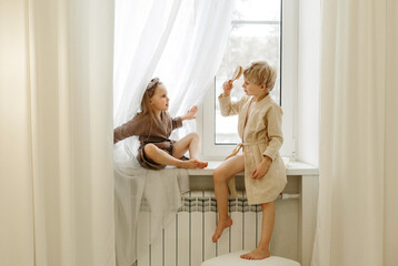 Obraz premium A boy and a girl are sitting on the windowsill in the bedroom, talking and playing