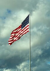 American flag on flagpole waving in the wind against clouds, blue sky