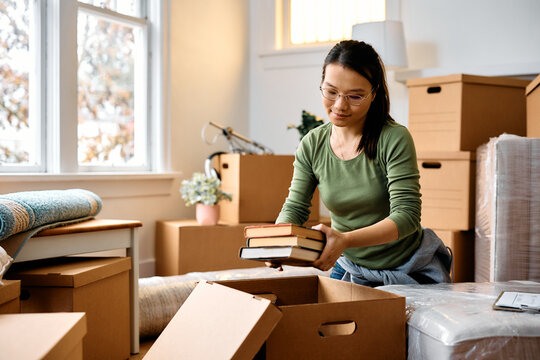 Young  Asian woman unpacking cardboard boxes while moving into new home.