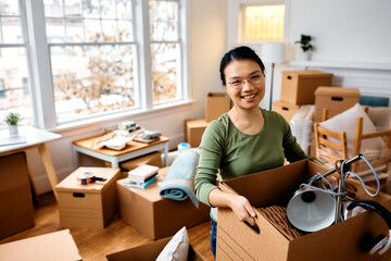 Happy Asian woman carrying her belongings into new home and looking at camera.