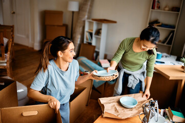 Happy female friends unpacking their belongings while moving into new home. - obrazy, fototapety, plakaty