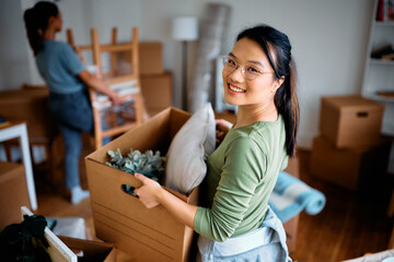 Young Asian woman moving into new home with her roommate and looking at camera.