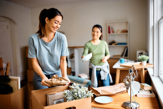 Happy woman and her female friend unpacking their belongings after moving into new apartment