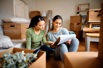 Young women going through housing plans after moving into their new home. - obrazy, fototapety, plakaty