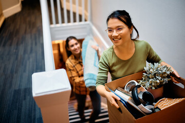 Happy Asian woman and her friend walking upstairs through hallway while moving in new apartment. - obrazy, fototapety, plakaty