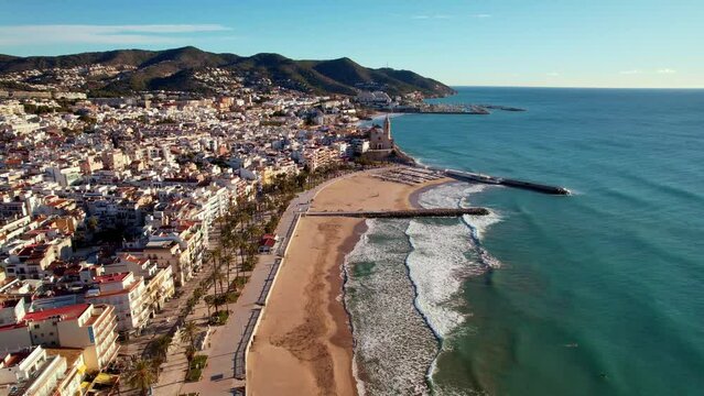 Aerial panoramic view of coastal village at seashore, old town, Sant Bartomeu i Santa Tecla de Sitges during sunny day in mediterranean town of Sitges, Province of Barcelona, Spain. Film intro. 4K