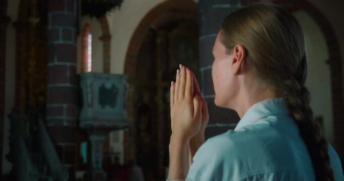 Woman head bowed in prayer to God in a dark corner of church. Folded hands in prayer to Christ the Redeemer.