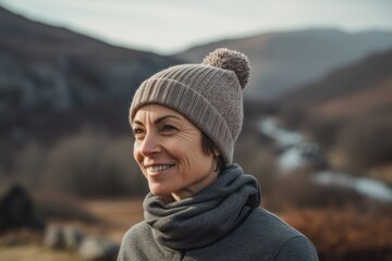 Portrait of a smiling middle-aged woman in a knitted hat and scarf standing in the mountains.