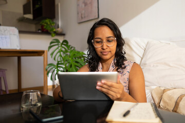 Serious Latin woman using digital tablet at home.
