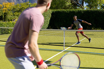 Obraz premium Happy diverse male friends playing tennis together at tennis court