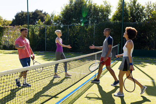 Happy diverse group of friends playing tennis, shaking hands at tennis court
