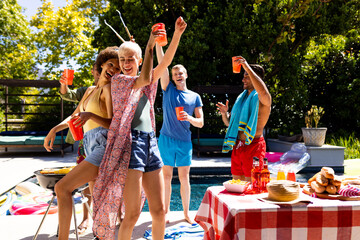 Happy diverse group of friends having pool party, barbecuing and dancing in garden