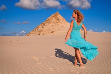 Beautiful blonde woman on hot sand with blue sky in the background. Photo taken on the shifting dunes over the Baltic Sea in Leba, Poland. Photo with a shallow depth of field with blurred background.