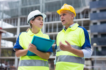Two builders in uniform planning their work in construction plant.