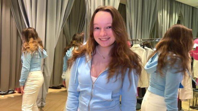 young teenage girl in dressing room dancing rejoices looking at herself in reflection in mirror wearing new clothes clothing store buying update shopping teens love clothes joy fun having fun in mall