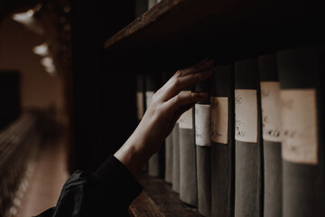 A girl picking an antique book on a shelf of a reading room in a library with her pale hand....