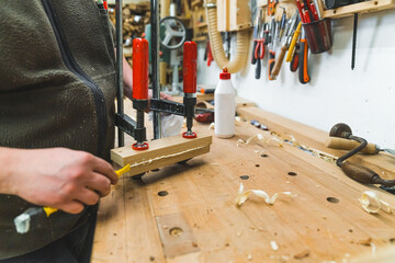 Carpenter during work. Woodworking expert glueing two wood pieces together with bar clamps. Indoor...